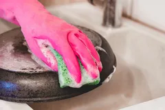 Afwassen van een pan met een schuurspons en roze handschoen in de gootsteen