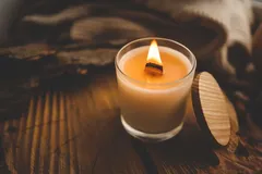 Brandende geurkaars in glazen pot op houten tafel, gezellig en sfeervol interieur.