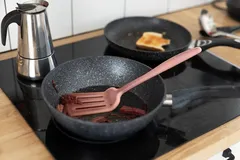 Koken op inductiefornuis met koekenpannen, gebakken ui en een koffiepannetje in keuken.